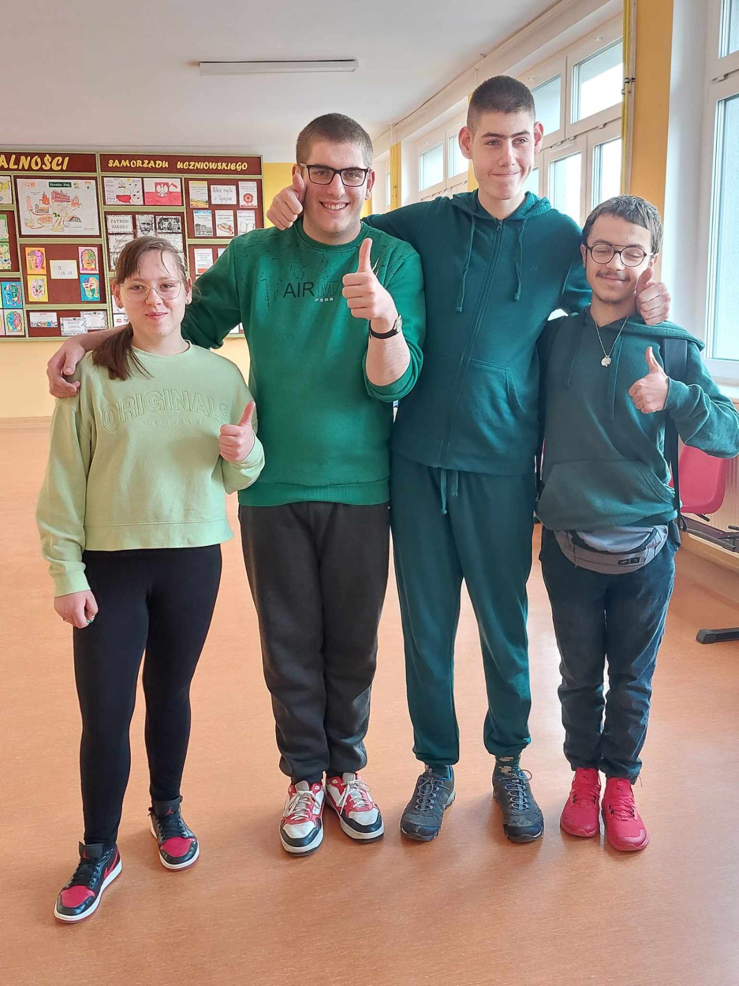 4 uczniów stoi na szkolnym korytarzu, są ubrani na zielono