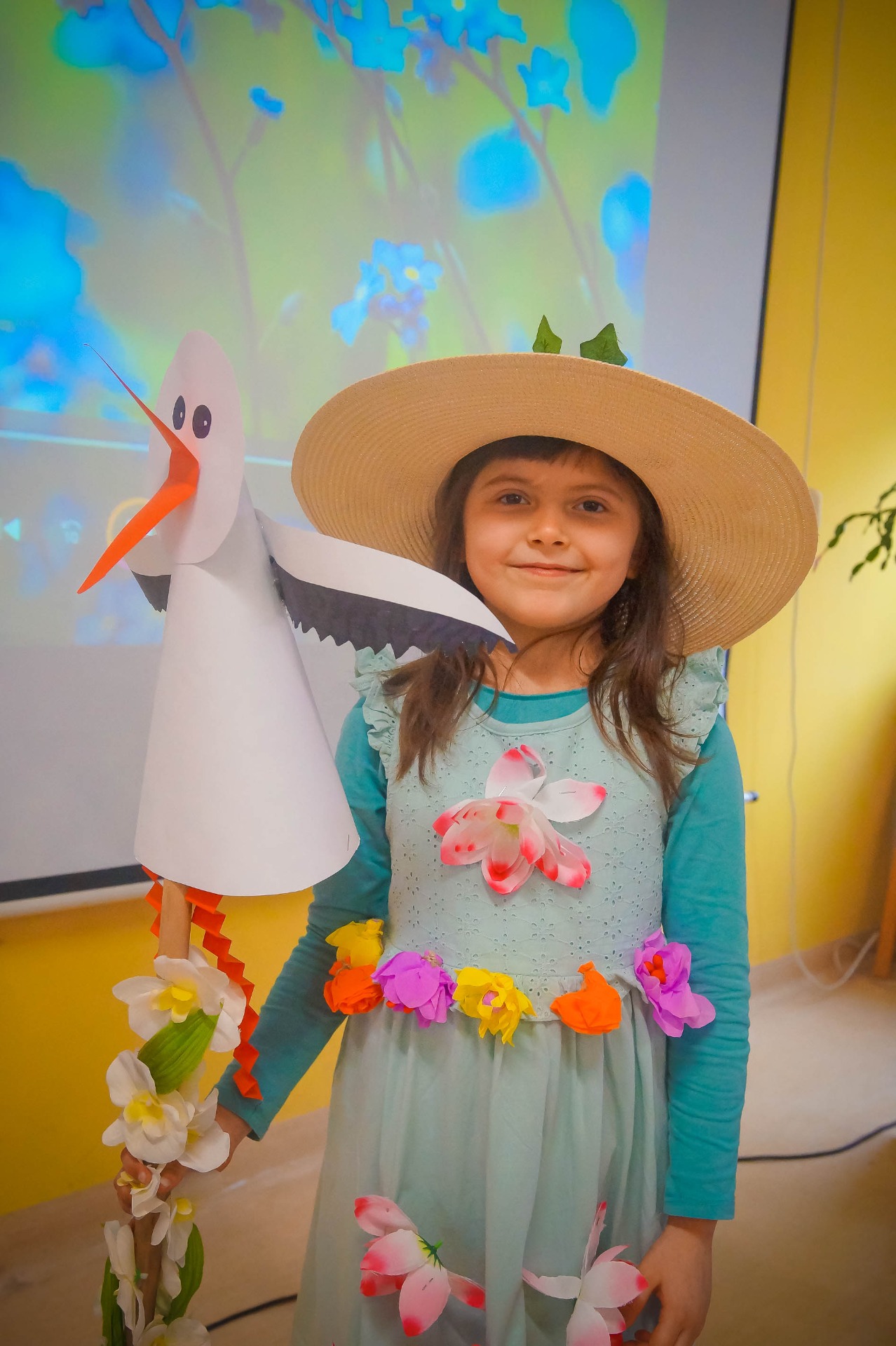 Mała dziewczynka w kapeluszu przebrana za wiosnę, w ręku trzyma kij z papierowym bocianem