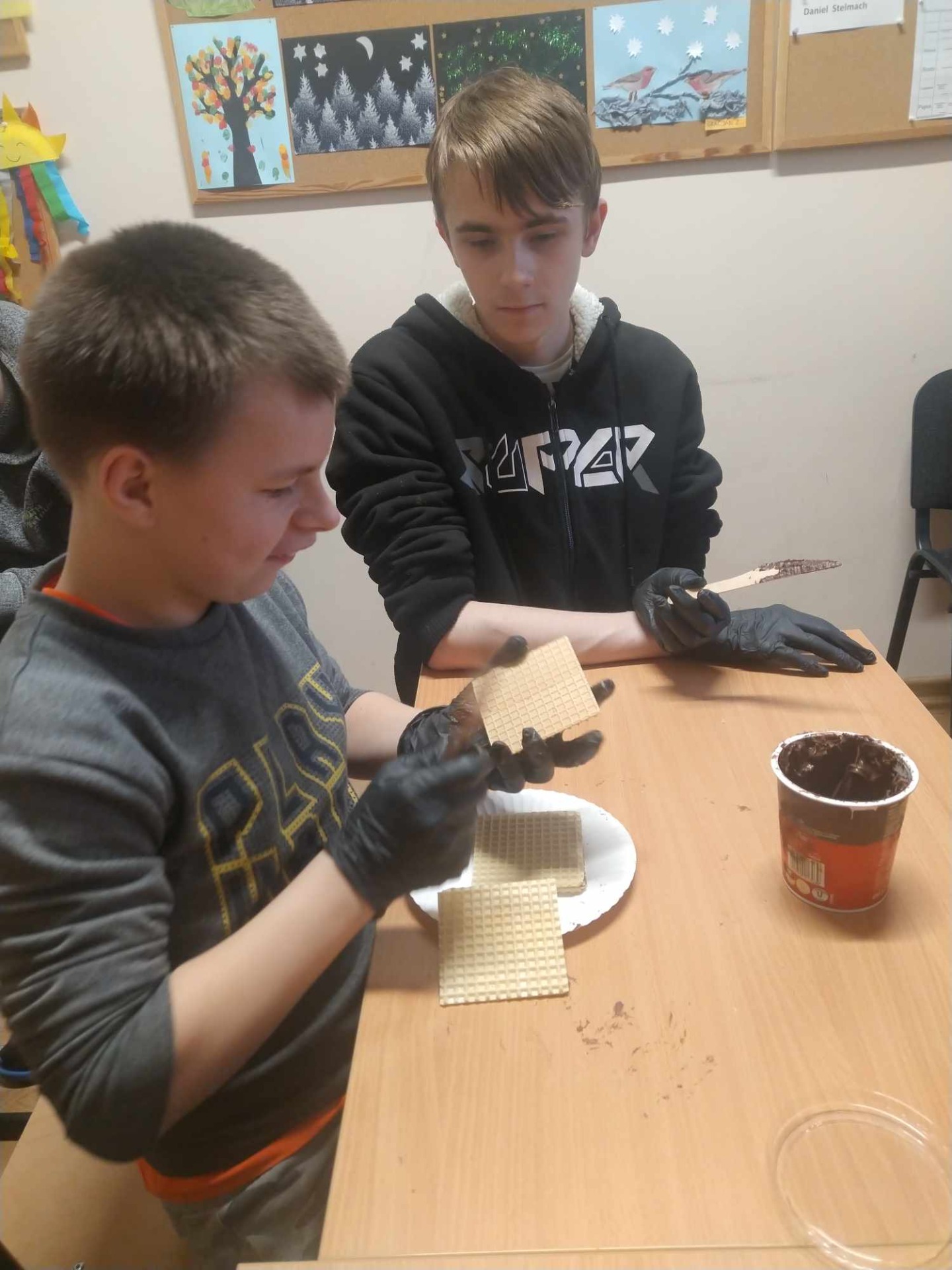 Chłopcy samodzielnie przygotowują wafle z czekoladą. Smarują nożami.
