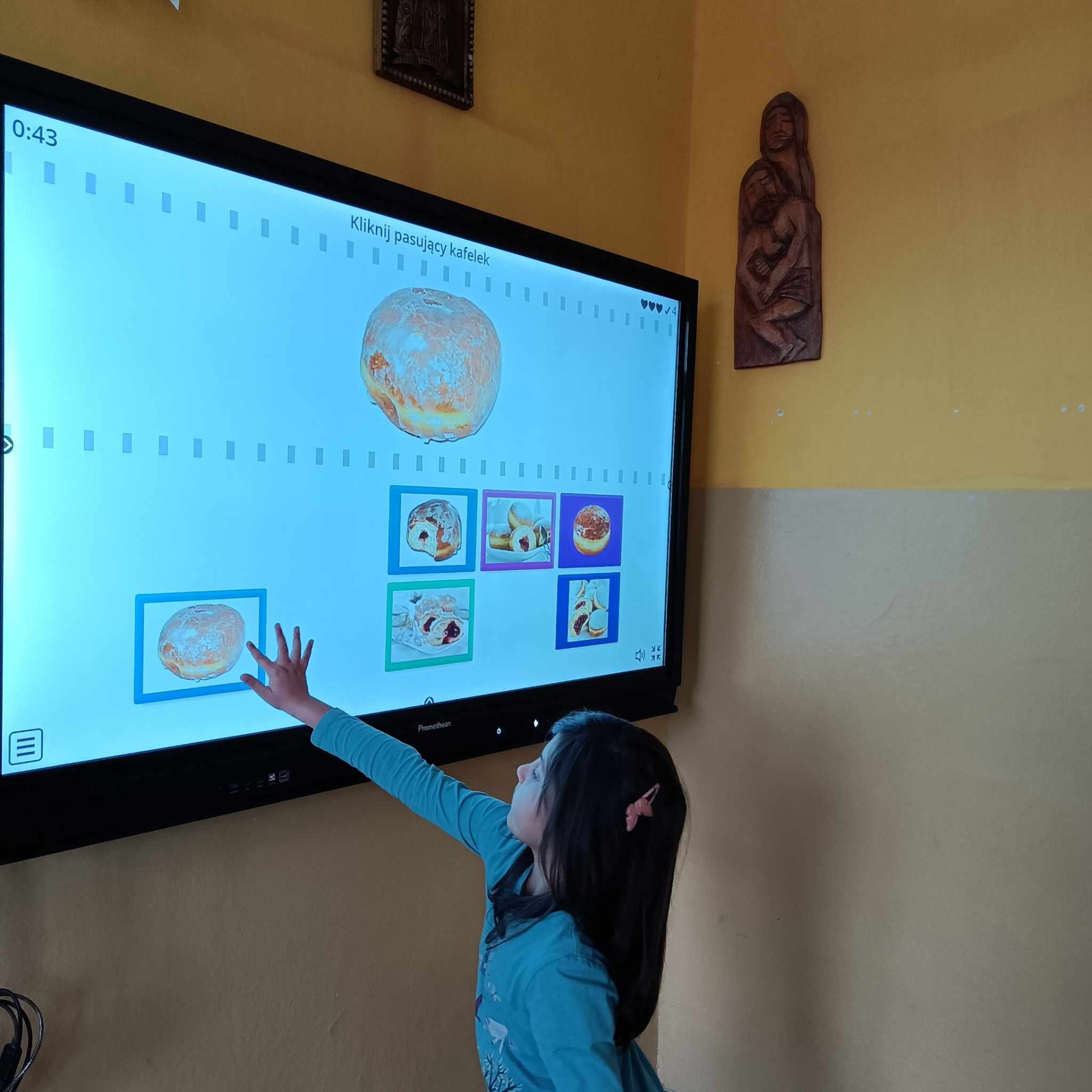 Uczennica korzysta z tablicy interaktywnej grające w grę dotyczącą pączków