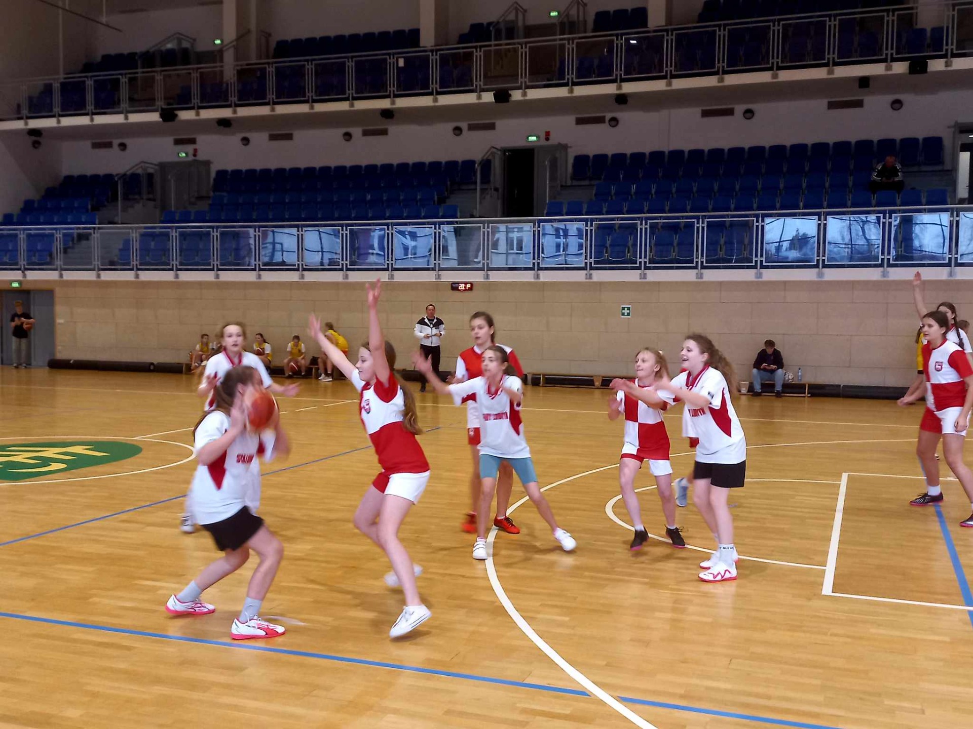Dziewczęta grają w koszykówkę w hali sportowej.