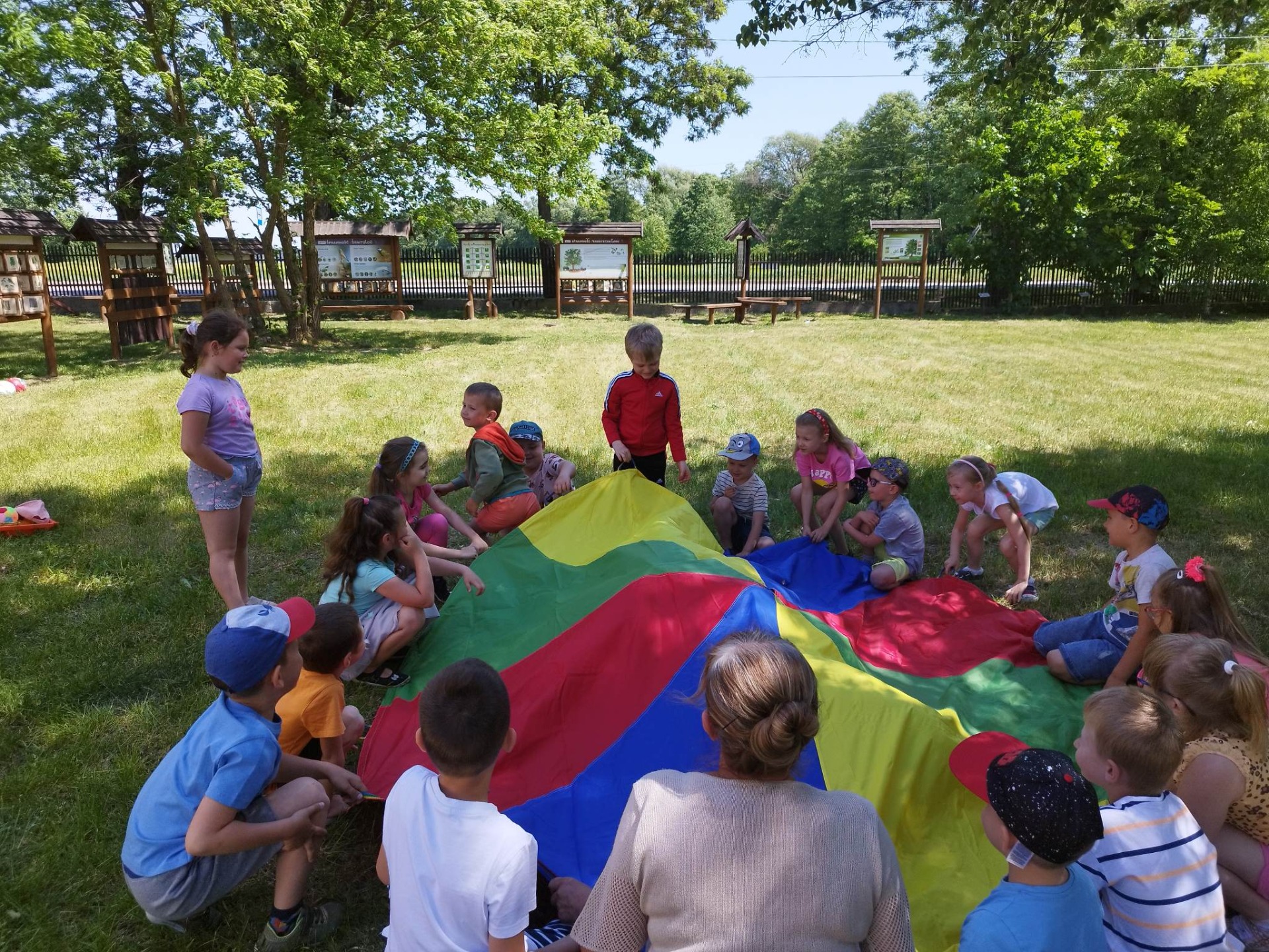 Grupa przedszkolaków bawi się chustą animacyjną na terenach zielonych przy szkole