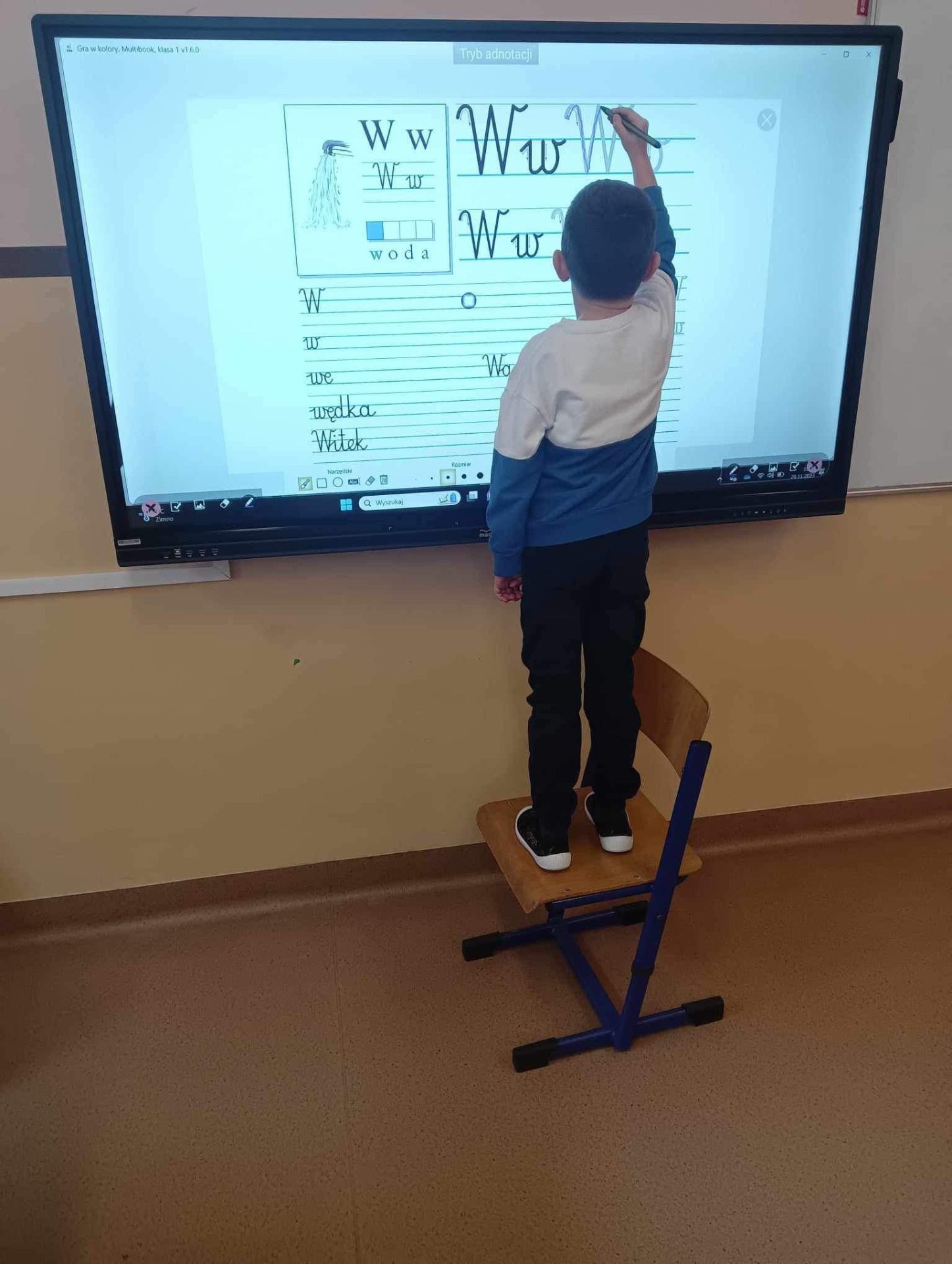 Uczeń klasy pierwszej pisze literki na nowym monitorze multimedialnym. 