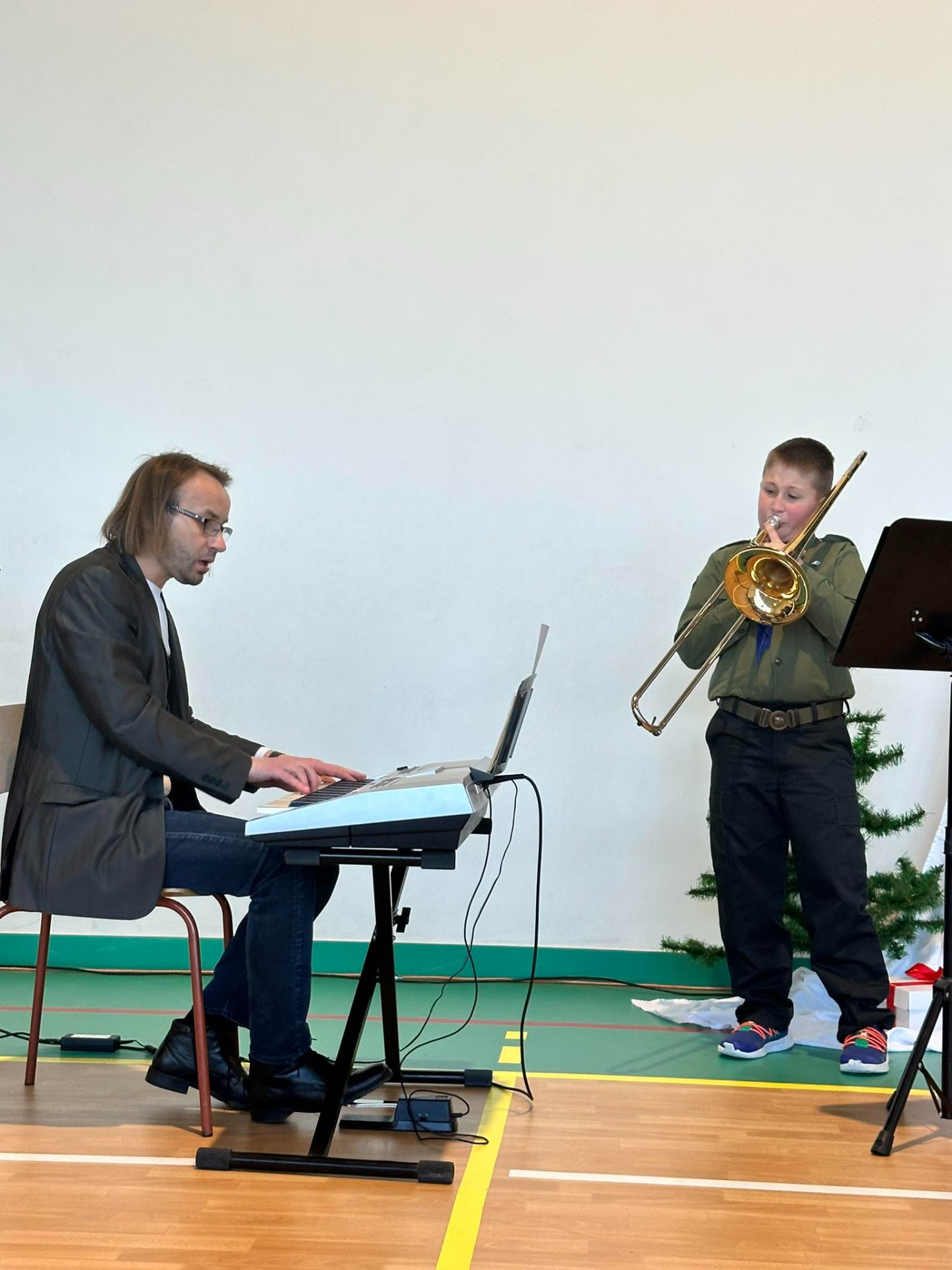 Zdjęcie przedstawia ucznia grającego na puzonie i akompaniującego mu nauczyciela.