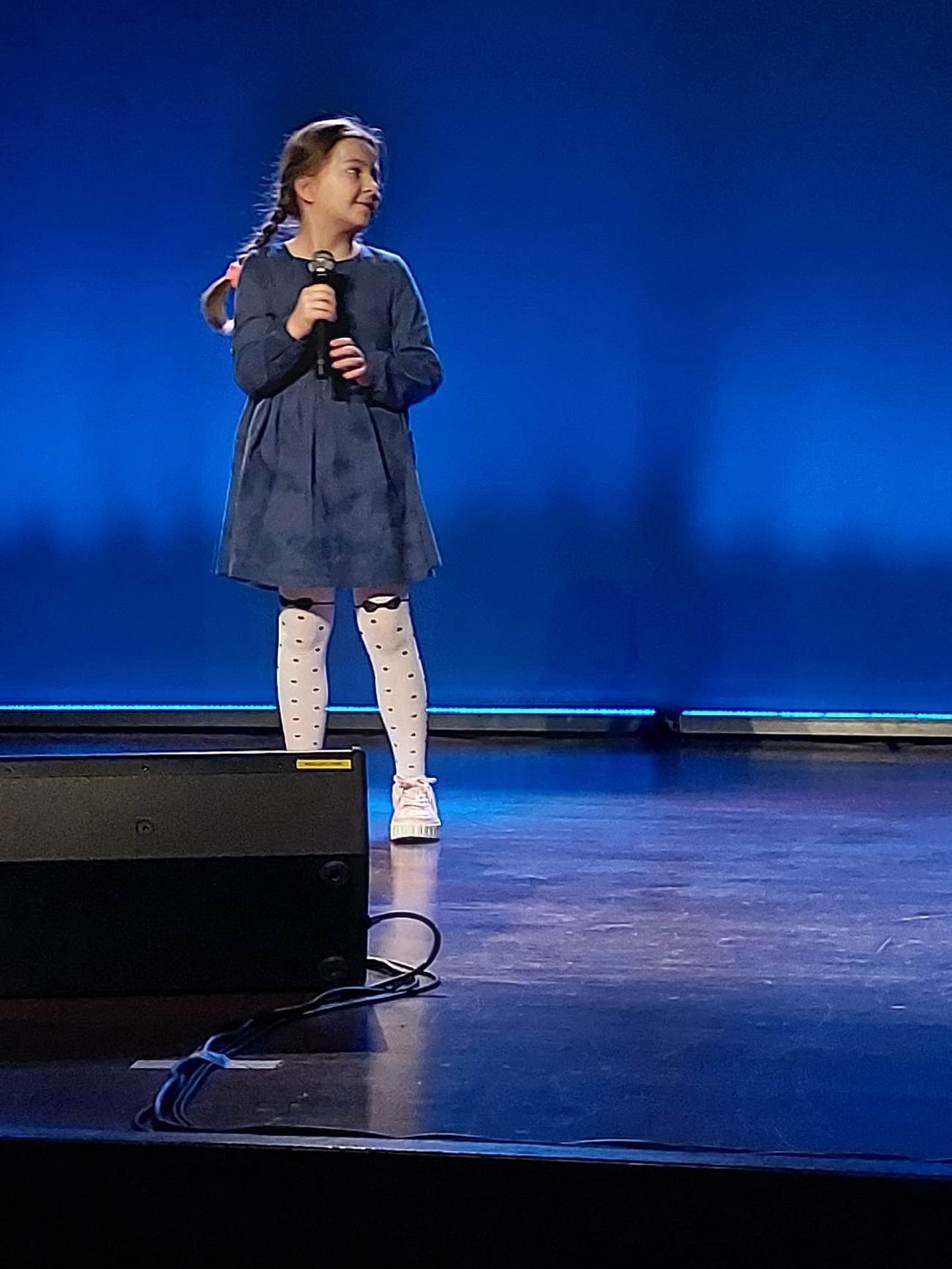 Dziewczynka z mikrofonem w ręku na scenie śpiewa piosenkę