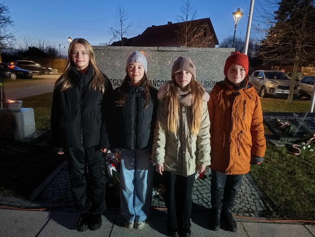 Grupa uczniów stoi przed pomnikiem.
