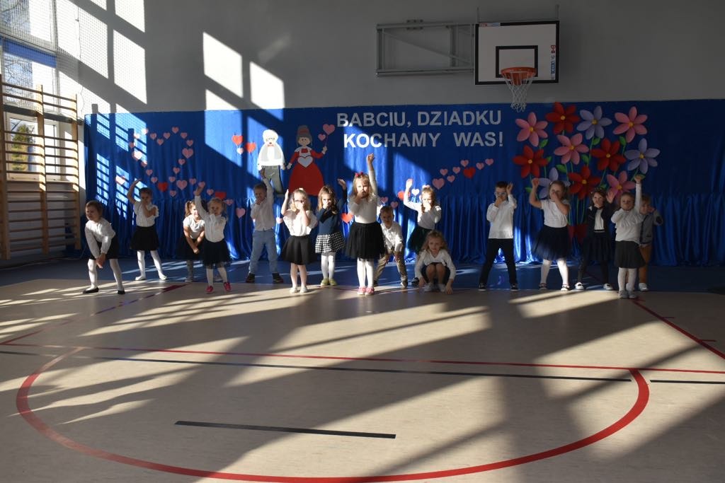 Uczniowie tańczą na sali gimnastycznej w czasie uroczystości z okazji Dnia Babci i Dziadka.