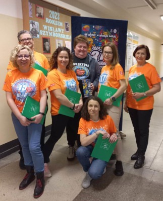 Wspólne zdjęcie nauczycieli biorących udział w imprezie, ubrani w pomarańczowe koszulki z logo WOSP stoją w grupce na korytarzu