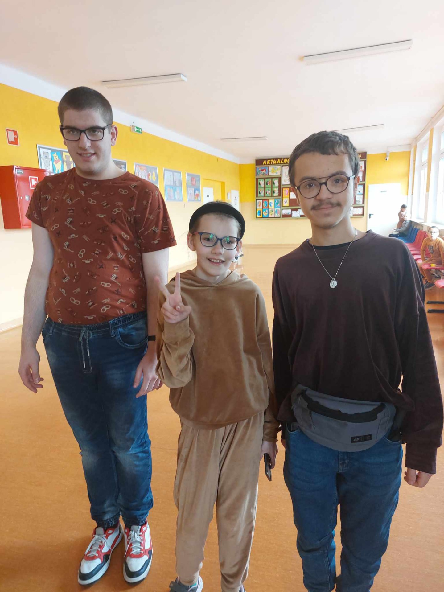 3 uczniów pozuje do zdjecia, mają brązowe ubrania