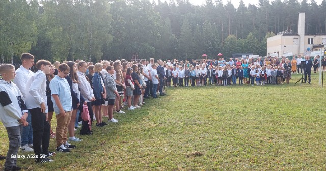 Grupa uczniów stoi na boisku szkolnym.